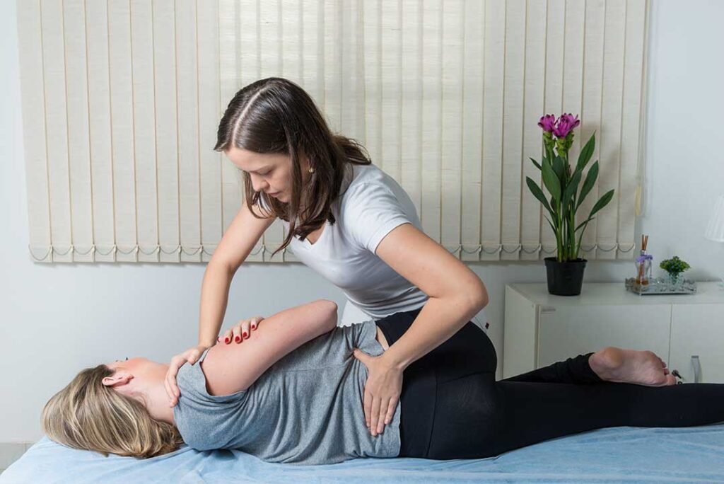 Clinician examining a patient’s back while discussing spinal movement in a bright treatment room.